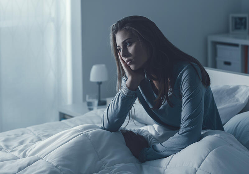 A woman sits awake on the edge of her bed in the middle of the night.