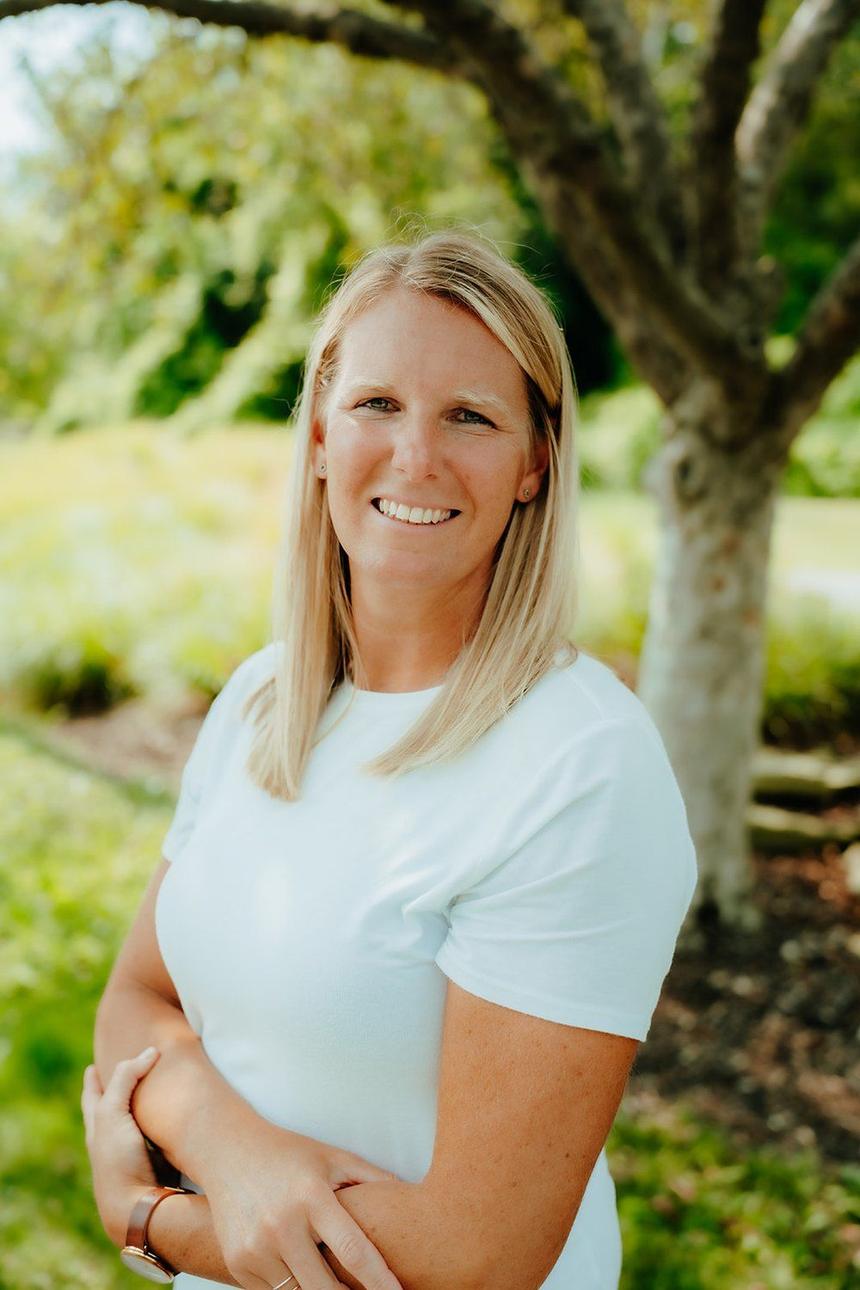 Anna Psaute standing outdoors under a tree, arms lightly folded, smiling.
