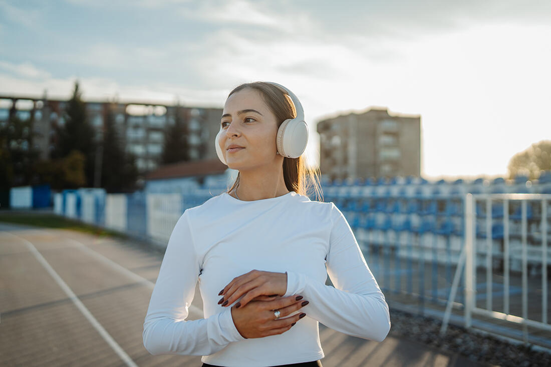 A young athlete stands on a running track at golden hour, arms folded across her chest.