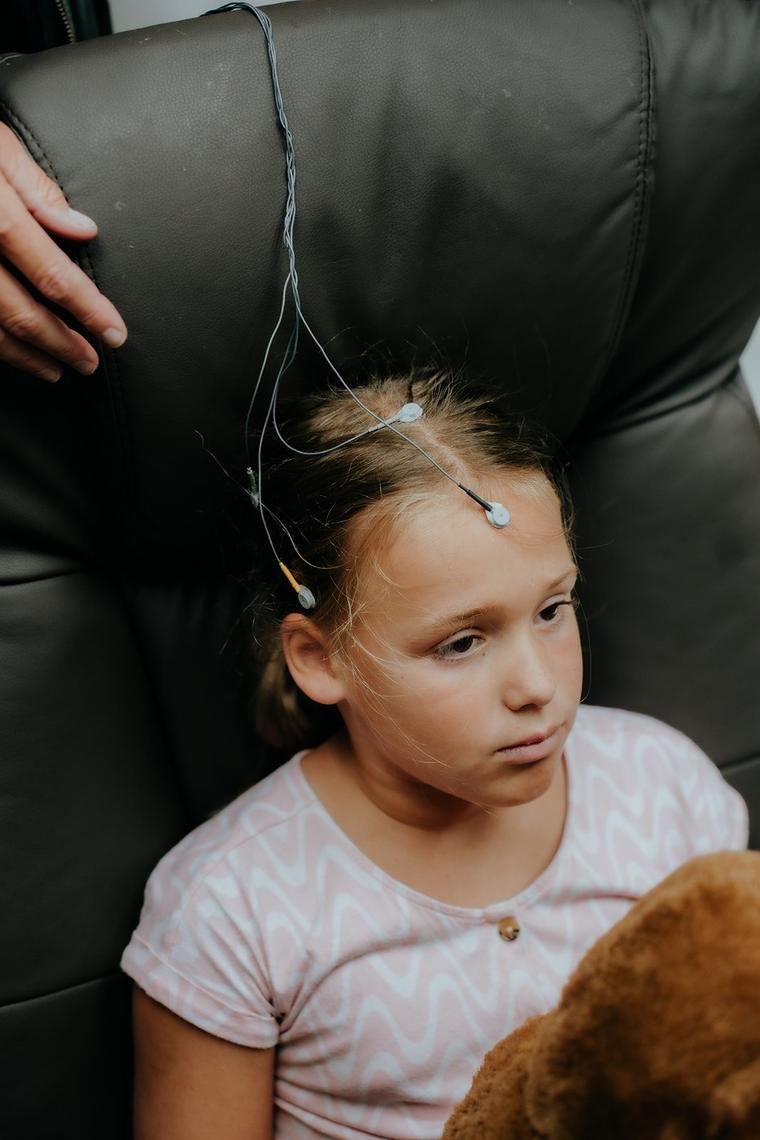 A young girl in the neurofeedback chair, fine sensor leads resting in her hair.